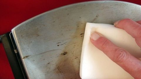 Eine Hand reinigt die schmutzige Sohle eines Bügeleisens mit einem Schmutzradierer, um Ablagerungen zu entfernen.