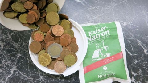 Silbermünzen liegen in einer Schüssel, während ein Päckchen Kaiser-Natron daneben steht, bereit zum Reinigen.
