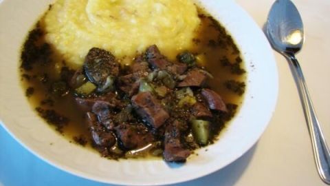 Ein Teller mit pikanten Nierchen in Sauce, serviert neben cremigem Kartoffelpüree, auf einem weißen Tisch mit Löffel.
