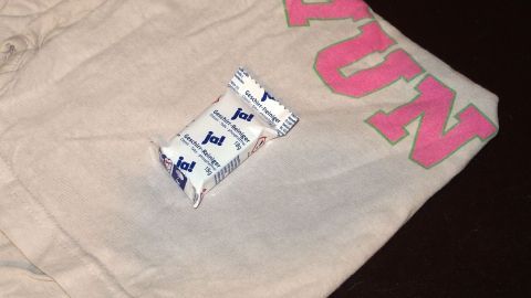 Kaffeeflecken aus T-Shirts vollständig und einfach entfernen. Ein beiges T-Shirt liegt auf einem dunklen Untergrund, daneben ein Spülmaschinentab, bereit zum Entfernen von Kaffeeflecken.
