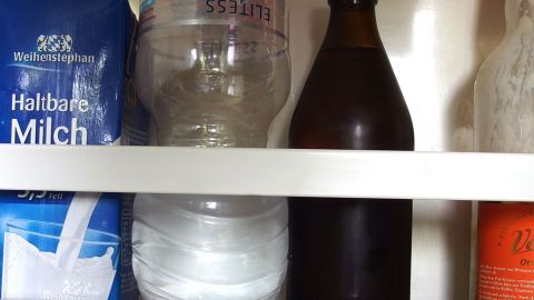 Eine geöffnete Flasche mit Kohlensäure steht im Kühlschrank neben einer transparenten Wasserflasche und Milch.