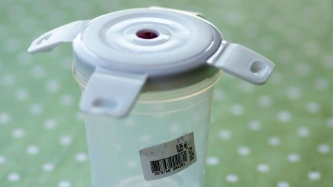 Ein transparenter Gefrierdosenbehälter steht auf einem grünen Punkttisch, während ein Aufkleber auf der Seite sichtbar ist.
