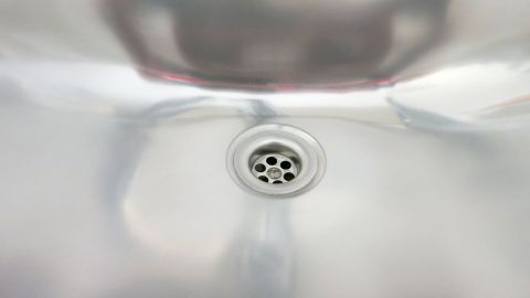 Eine glänzende Spüle reflektiert Licht und zeigt einen Abfluss in der Mitte, umgeben von einer sauberen Küchenumgebung.
