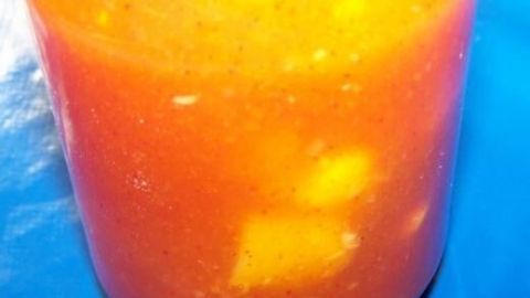 Ein Glas mit süß-scharfem Mango-Chutney steht auf einem blauen Untergrund, gefüllt mit gelben Mangostücken.