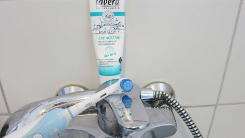Ein Reinigungsspray steht auf einem Wasserhahn, während eine Bürste daneben liegt, um Kalk- und Rostflecken zu entfernen.