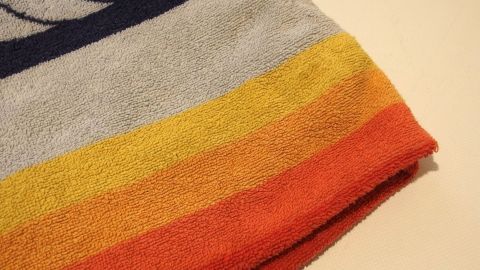 Ein gestreiftes Handtuch mit seifiger Wäsche liegt ordentlich gefaltet auf einem hellen Tisch und zeigt lebendige Farben.
