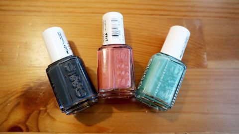 Mithilfe von Eisspray kann man Nagellack ruckzuck hart werden lassen. Drei Nagellackflaschen in verschiedenen Farben stehen auf einem Holztisch, bereit zum schnellen Trocknen mit Eisspray.