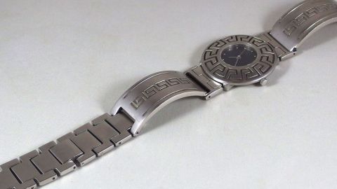 Ein Metall-Uhrenarmband wird auf einem weißen Hintergrund betrachtet, um es mit Zahnpasta und Zahnbürste zu reinigen.