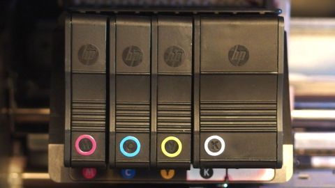 Tintenpatronen in einem Drucker, sortiert nach Farben (Magenta, Cyan, Gelb, Schwarz) und markiert mit entsprechenden Symbolen.