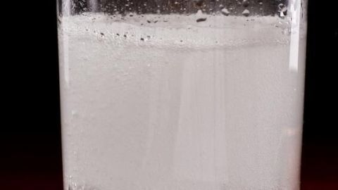 Ein Glas enthält sprudelndes Wasser mit Alka-Seltzer auf einem dunklen Holztisch.