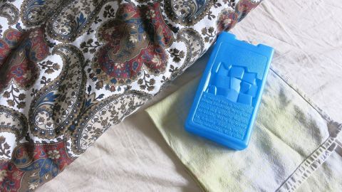 Ein blauer Kühlakku liegt auf einem Bett, um eine Abkühlung während heißer Nächte zu bieten. Der Stoff ist gemustert.