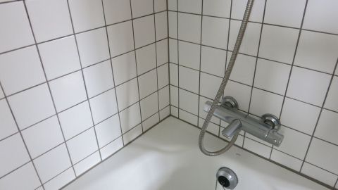 Weiße Kacheln in einer Dusche sind sichtbar, während Wasser aus der Duschbrause fließt, um sie zu reinigen.