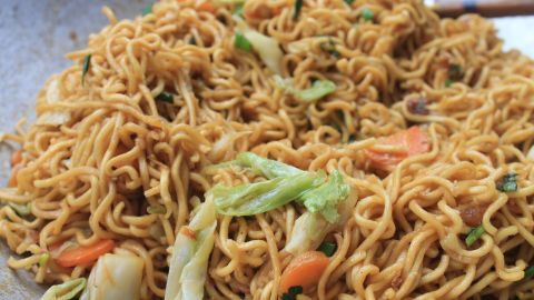 Mie-Nudeln liegen frisch zubereitet in einer Pfanne, umgeben von buntem Gemüse wie Karotten und Kohl, appetitlich angerichtet.