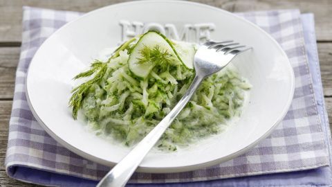 Ein frischer Gurkensalat liegt in einer weißen Schüssel auf einem karierten Tischläufer und wartet auf den Verzehr.