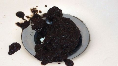 Ein großer Klumpen Kaffeesatz liegt in einem Abfluss, während er beginnt, sich zu verstopfen.
