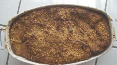 Ein Ofenschlupfer in einer ovalen Auflaufform ruht frisch gebacken auf weißen Fliesen, bedeckt mit knuspriger Kruste.