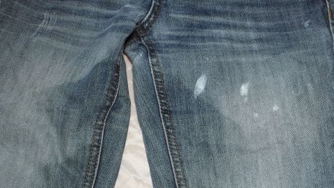 Jeans mit Farbspritzern auf der Vorderseite liegen auf einer hellen Oberfläche, die Abnutzungsspuren zeigt.