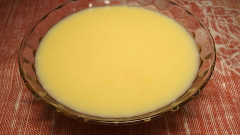 Ein gläserner Schüssel mit flüssigem Pudding steht auf einer rustikalen Tischoberfläche, bereit zum Festwerden.
