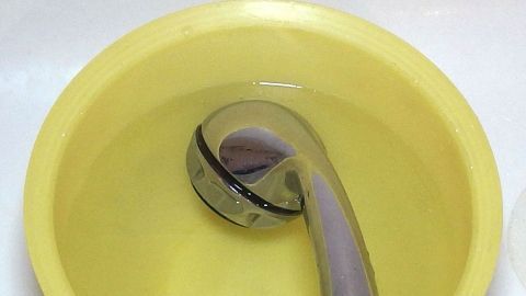 Ein verkalkter Duschkopf liegt in einem gelben Behälter mit Wasser und wird zur Entkalkung vorbereitet.