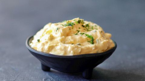 Ein cremiger Eierdip in einer schwarzen Schüssel, garniert mit frischen Kräutern, auf einer grauen Oberfläche.
