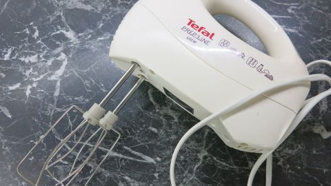 Man sollte Teig nicht länger als insgesamt 2 Minuten rühren. Ansonsten wird zu viel Luft untergeschlagen. Ein Handmixer liegt auf einer marmorierten Arbeitsfläche, bereit, Teig zu bearbeiten und ideal für das Backen.
