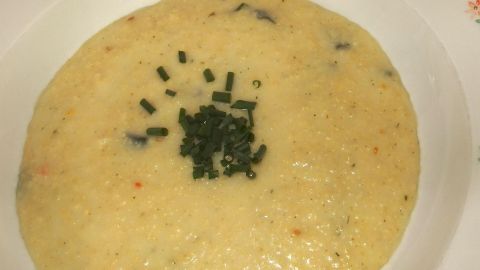 Eine cremige Hirsesuppe liegt in einer Schale, garniert mit frischem Schnittlauch in einer einfachen Küchenszene.
