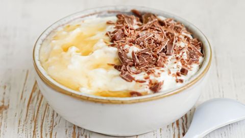 Eine Schüssel mit cremigem Dessert, überzogen mit Schokoladenspänen, steht auf einem rustikalen Holzuntergrund.