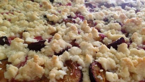 Ein Zwetschgenkuchen mit goldbraunem Streusel liegt auf einem Blech, umgeben von frischen Zwetschgen und duftet köstlich.
