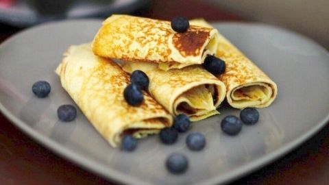 Vegane Crepes sind auf einem herzförmigen Teller angerichtet und mit frischen Heidelbeeren dekoriert.