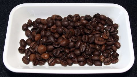 Dunkle Kaffeebohnen liegen in einer weißen Schale auf einem schwarzen Untergrund, bereit für den Kauf.