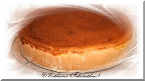 Ein goldbrauner Quarkkuchen kühlt auf einem Gitter ab, leicht in Plastikfolie eingewickelt. Text: © Catharina (Internekhaas).