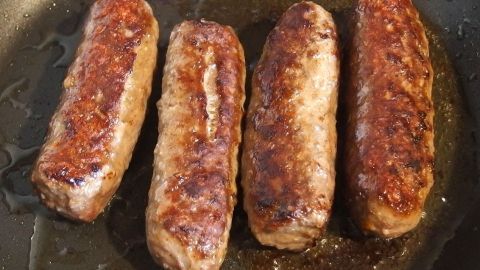 Cevapcici braten in einer Pfanne, gleichmäßig goldbraun gebräunt, bereit zum Servieren in einer klassischen Küche.