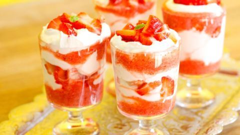 Vla-Flip wird in transparenten Gläsern serviert, mit Erdbeeren und Sahne, vor einem gelben Hintergrund.