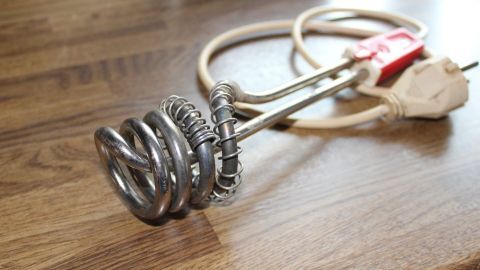 Ein Tauchsieder liegt auf einer Holzoberfläche. Er hat eine spiralförmige Heizspirale mit einem elektrischen Kabel angeschlossen.