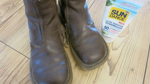 Verleihe deinen Lederschuhen neuen Glanz mit einem ungewöhnlichen Trick – Sonnenmilch! Dieser clevere Hack pflegt das Leder und schützt es vor dem Austrocknen. Perfekt für geschmeidige, glänzende Schuhe im Alltag. Braune Lederschuhe stehen auf Holzboden, neben ihnen befindet sich eine Tube "SUN DANCE MED ULTRA SENSITIVE SONNENBALSAM 50 HOCH".