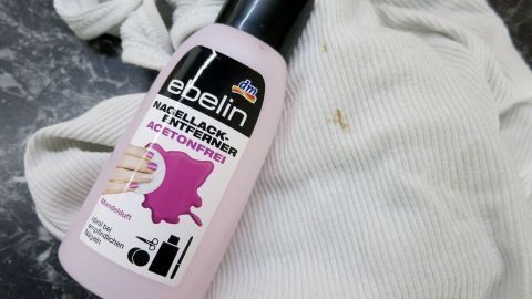 Ein Fläschchen Nagellackentferner steht auf einem weißen Tuch, das möglicherweise Harzflecken aufweist.