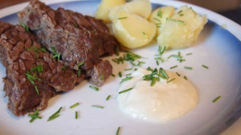 Zarte Klopse liegen neben Kartoffeln und einer cremigen Meerrettichsoße auf einem weißen Teller, garniert mit Schnittlauch.