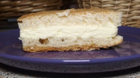 Ein St&uuml;ck Bienenstich liegt auf einem blauen Teller und zeigt die helle F&uuml;llung zwischen den Teigschichten.