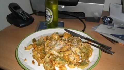 Geschmelzte Maultaschen liegen auf einem Teller, während ein Bier daneben steht; der Hintergrund zeigt einen unordentlichen Tisch.