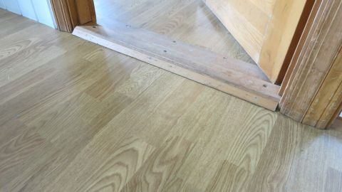 Laminatboden mit Weichspüler im Wischwasser pflegen: Der Boden glänzt danach und sieht richtig gut aus. Ein glänzender Laminatboden wird durch Weichspüler gepflegt, während eine Tür zum nächsten Raum offen steht.