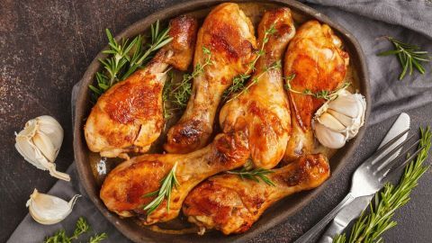 Zartes Hähnchenfleisch ist in einer Schale angerichtet, umgeben von frischen Kräutern und Knoblauchzehen.