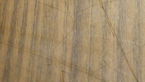 Mit einer halbierten Haselnuss Kratzer aus Holzmöbeln beseitigen. Ein Holzmöbelstück zeigt mehrere Kratzer, die durch Gebrauchsspuren entstanden sind, in einem wohnlichen Raum.