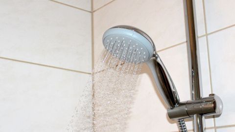 Ein Duschkopf sprüht Wasser in einem modernen Badezimmer. Der Fokus liegt auf dem Wasserverbrauch, um Ressourcen zu sparen.