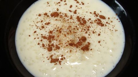 Ein cremiger Milchbrei in einer schwarzen Schüssel, garniert mit Zimt, wird zum Genuss serviert.