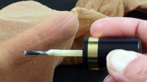 Ein Nagellackfläschchen wird gehalten, während eine Laufmasche in einem feinen Nylonstrumpf sichtbar ist.