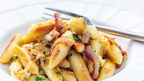 Saftige Schupfnudeln werden mit knusprigem Schinken und Zwiebeln auf einem weißen Teller serviert.