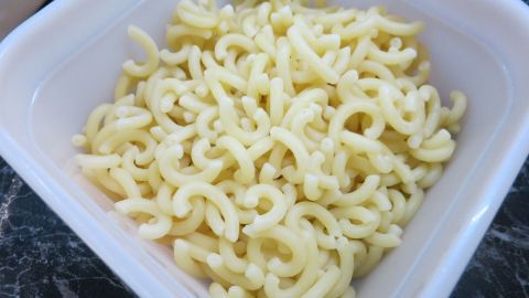 Gekochte Nudeln liegen in einer weißen Schüssel auf einer dunklen Marmoroberfläche.
