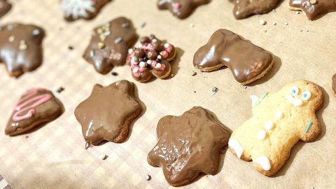 Schokoladeneingetauchte Butterplätzchen werden kunstvoll mit Zuckerguss verziert, umgeben von weiteren dekorativen Keksen.