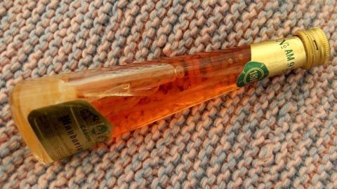 Eine Flasche Schnaps liegt schräg auf einem warmen Tuch, das zur Linderung von Ohrenschmerzen verwendet wird.