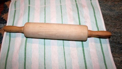 Ein Holztaisenroller liegt auf einem gestreiften Küchentuch, bereit zum Ausrollen von Teig gegen Mandelentzündung und Halsschmerzen.